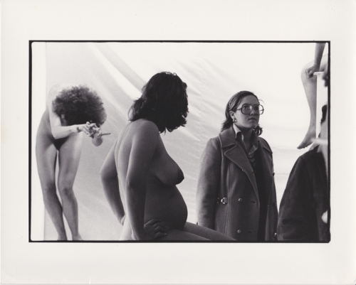 Detail view of Women in Glasses art exhibition showing a viewer looking past nude pregnant model and another posing model in the background.