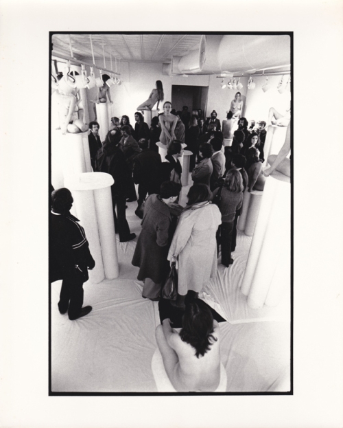 Installation view of 1976 show Women in Glasses: audience meandering around nude women on pedestals with eye glasses.